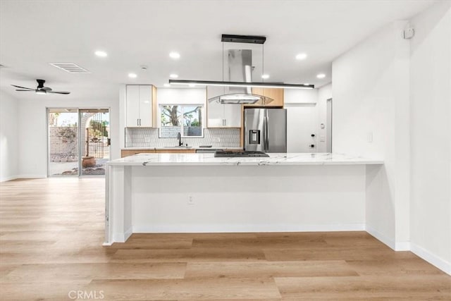 kitchen featuring light wood finished floors, tasteful backsplash, appliances with stainless steel finishes, a peninsula, and white cabinetry