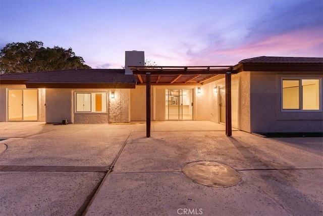 back of house at dusk featuring a patio and stucco siding