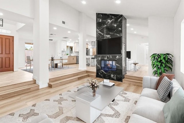 living area with light wood-type flooring, a fireplace, high vaulted ceiling, and recessed lighting