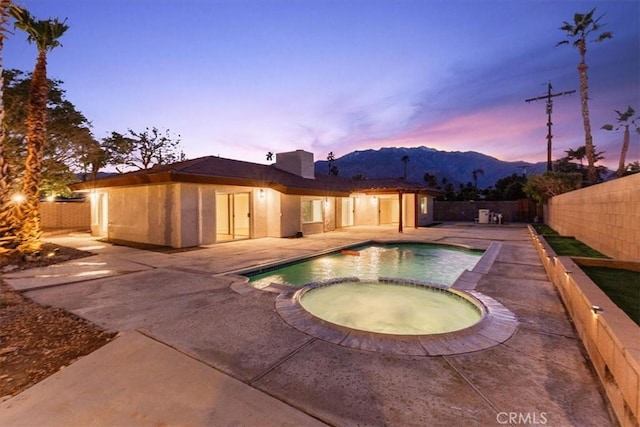 pool at dusk with a pool with connected hot tub, a patio area, and a fenced backyard