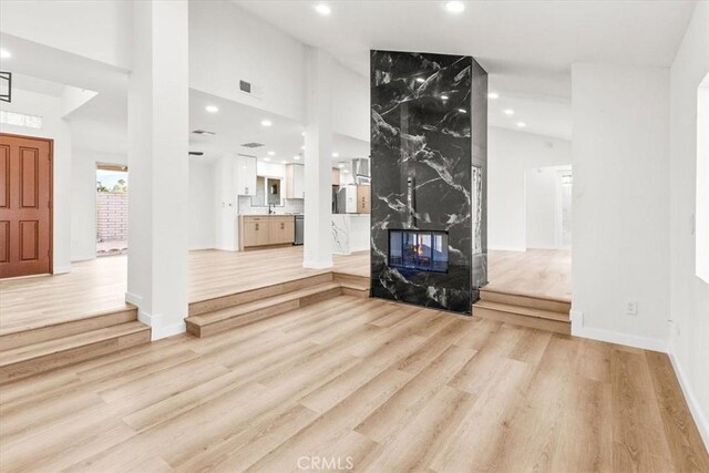 unfurnished living room with light wood-style flooring, a fireplace, a towering ceiling, and recessed lighting