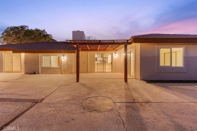 back of property at dusk with a patio area and stucco siding