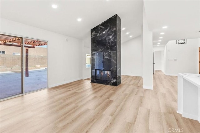 unfurnished living room featuring light wood-style flooring, a premium fireplace, baseboards, and recessed lighting