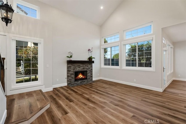 unfurnished living room with a chandelier, high vaulted ceiling, a fireplace, wood finished floors, and baseboards