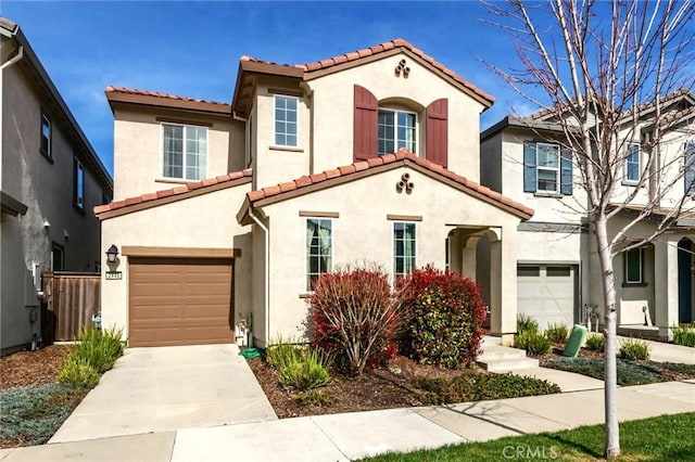 mediterranean / spanish-style home featuring a garage, driveway, a tiled roof, and stucco siding