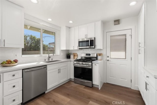 kitchen featuring wood finished floors, appliances with stainless steel finishes, a sink, and white cabinetry