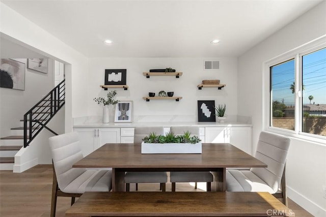 dining area with light wood-style flooring, stairs, visible vents, and baseboards