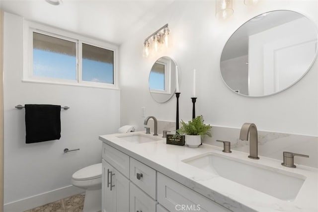 full bath featuring baseboards, a sink, toilet, and double vanity