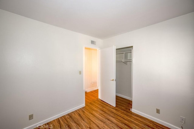 unfurnished bedroom featuring baseboards, a closet, visible vents, and wood finished floors