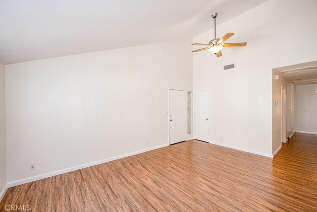 empty room featuring baseboards, visible vents, a ceiling fan, light wood-style flooring, and high vaulted ceiling