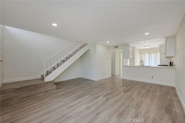 unfurnished living room with recessed lighting, a sink, light wood-type flooring, baseboards, and stairs