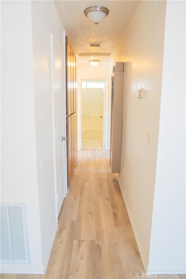 corridor featuring light wood finished floors, visible vents, and baseboards