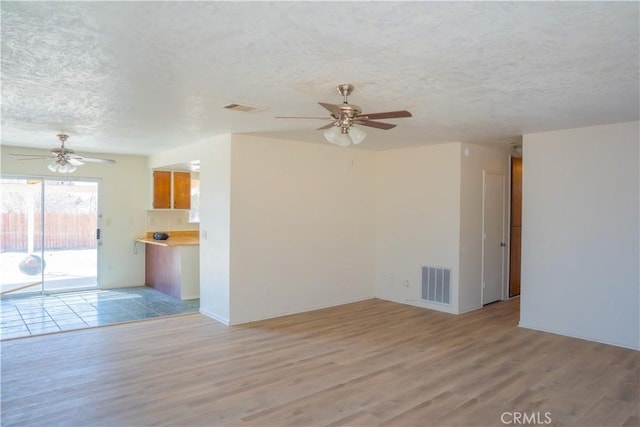 unfurnished living room with light wood-style floors, visible vents, and a textured ceiling