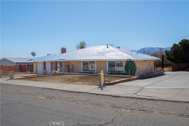 ranch-style home with a fenced front yard, a chimney, stucco siding, concrete driveway, and an attached garage