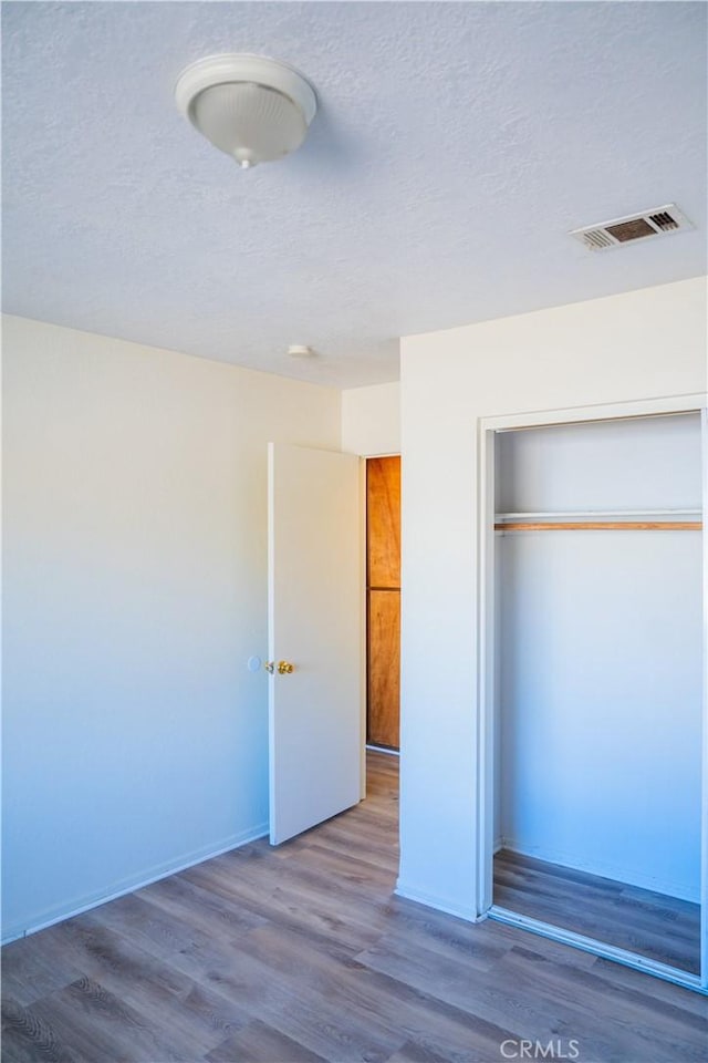 unfurnished bedroom with a closet, visible vents, a textured ceiling, and wood finished floors