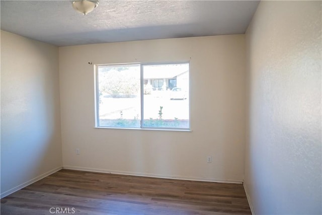 empty room with a textured ceiling, baseboards, and wood finished floors