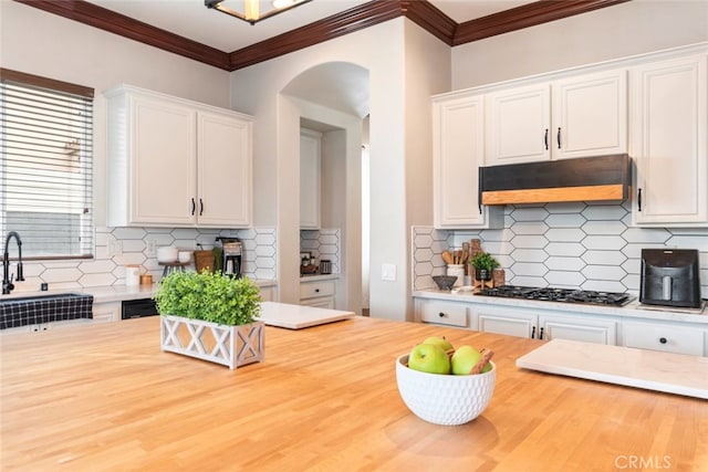 kitchen with tasteful backsplash, stainless steel gas stovetop, white cabinetry, butcher block countertops, and under cabinet range hood