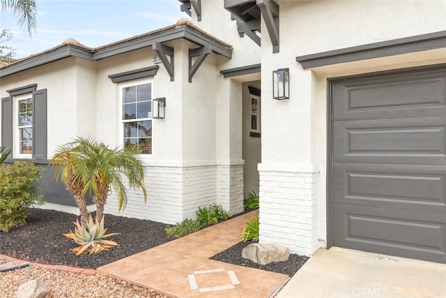 entrance to property featuring brick siding, an attached garage, and stucco siding