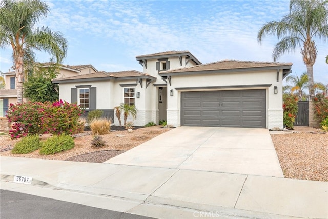 prairie-style house featuring an attached garage, stucco siding, concrete driveway, and brick siding