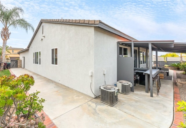 rear view of property with a patio area, fence, central AC unit, and stucco siding