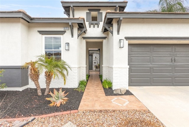 view of exterior entry featuring a gate, brick siding, an attached garage, and stucco siding