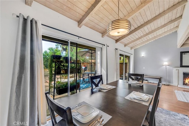 dining room with vaulted ceiling with beams, wood finished floors, wood ceiling, baseboards, and a lit fireplace