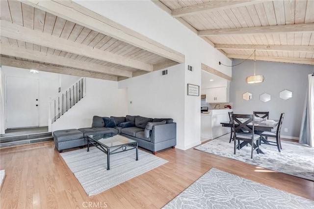 living area with vaulted ceiling with beams, light wood finished floors, stairway, wood ceiling, and baseboards