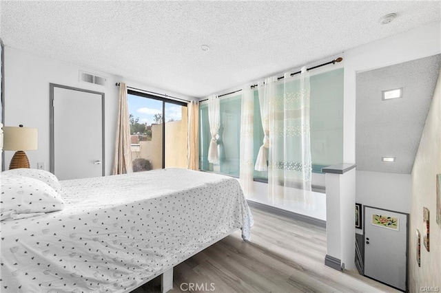 bedroom featuring a textured ceiling, access to outside, wood finished floors, and visible vents