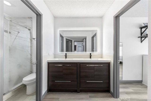 bathroom with toilet, a textured ceiling, a marble finish shower, and a sink