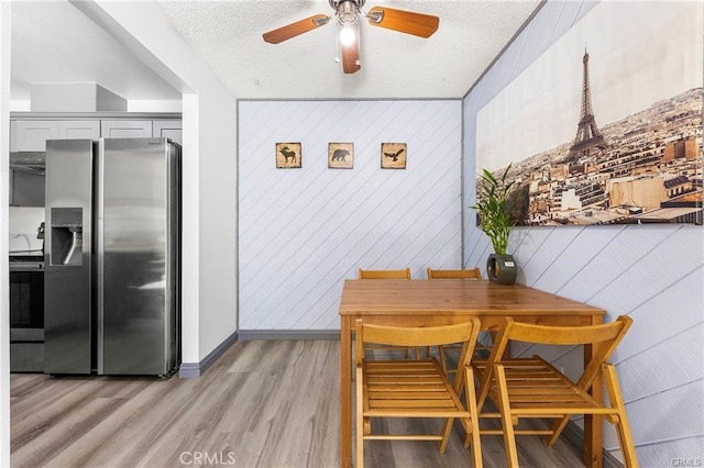 dining space with a textured ceiling, light wood-type flooring, a ceiling fan, and baseboards