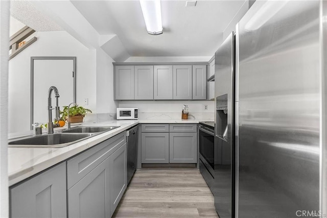 kitchen featuring stainless steel appliances, light wood-style floors, a sink, and gray cabinetry