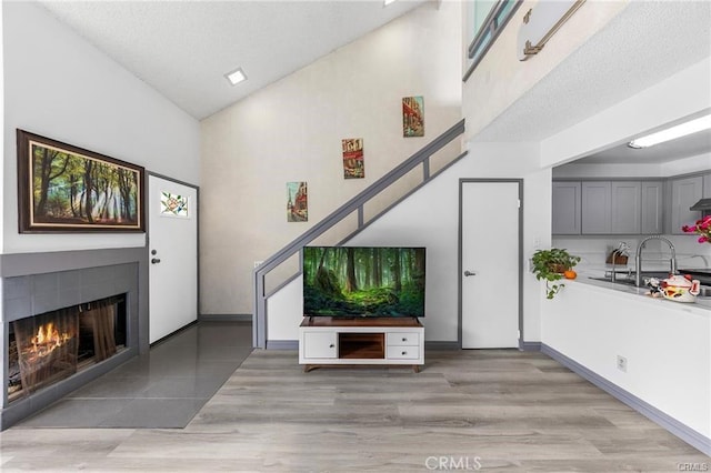 unfurnished living room featuring high vaulted ceiling, light wood finished floors, a tiled fireplace, and a sink