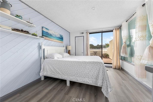 bedroom featuring access to outside, visible vents, a textured ceiling, and wood finished floors