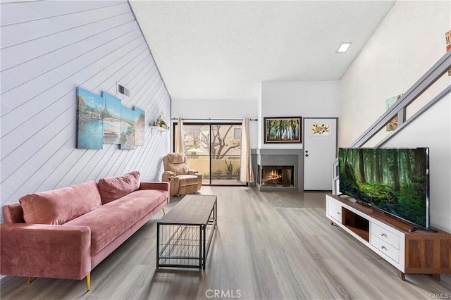 living room featuring lofted ceiling, a lit fireplace, wood finished floors, and visible vents