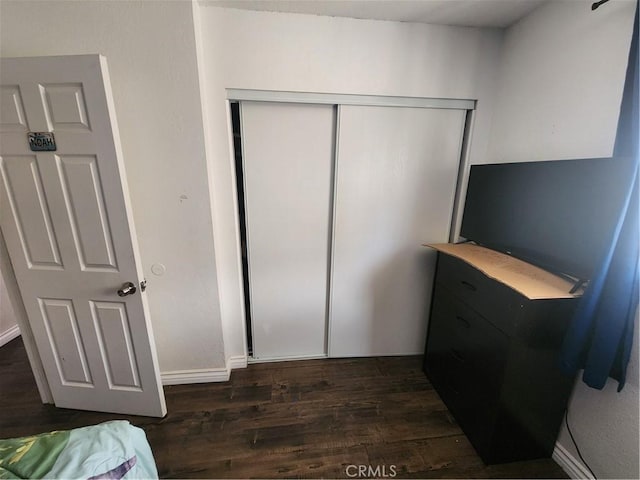 bedroom with a closet, dark wood finished floors, and baseboards