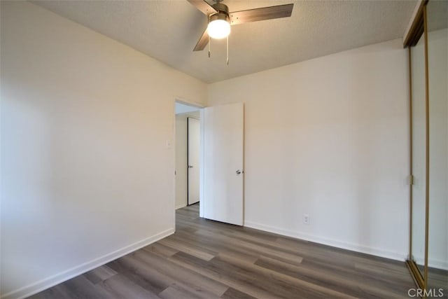 empty room featuring a textured ceiling, dark wood-type flooring, a ceiling fan, and baseboards