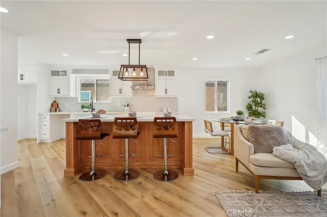 bar featuring wall chimney exhaust hood, light wood finished floors, recessed lighting, and tasteful backsplash