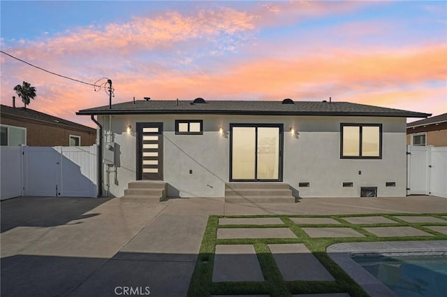 back of house at dusk with entry steps, a patio, crawl space, a gate, and stucco siding