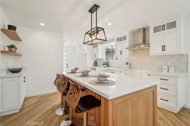 kitchen featuring glass insert cabinets, white cabinets, a kitchen island, light wood-type flooring, and wall chimney exhaust hood