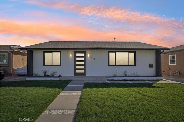 ranch-style house with a front lawn, a shingled roof, and stucco siding