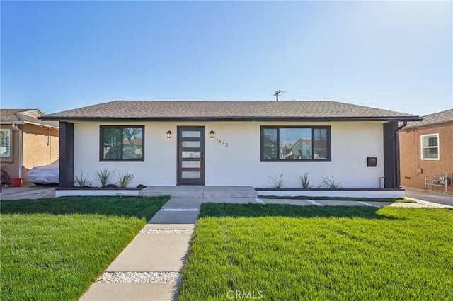 view of front of property with a front yard, roof with shingles, and stucco siding