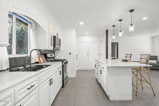 kitchen featuring stainless steel appliances, backsplash, white cabinetry, a sink, and a kitchen bar