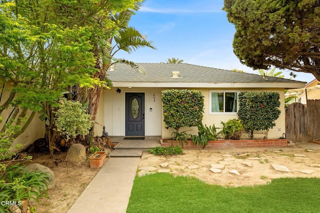 view of front of home with stucco siding, fence, and roof with shingles