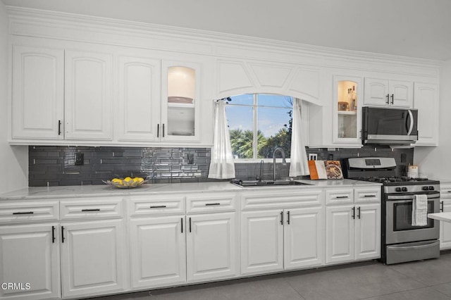 kitchen featuring white cabinets, stainless steel appliances, a sink, decorative backsplash, and glass insert cabinets