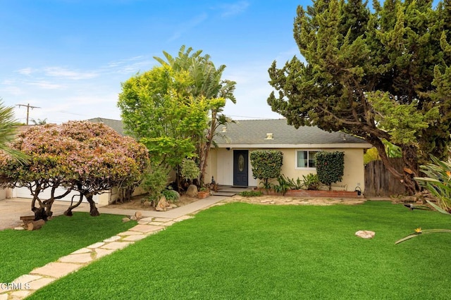 ranch-style home with stucco siding, fence, roof with shingles, and a front yard