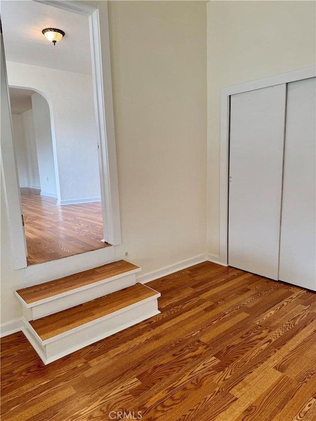 interior space with baseboards, a closet, arched walkways, and wood finished floors