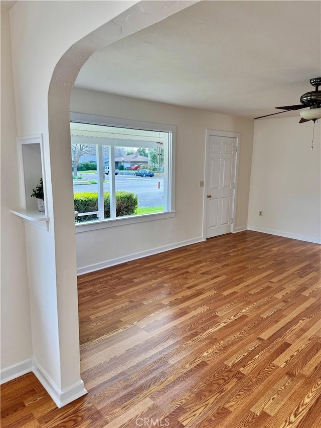 unfurnished room with light wood-style floors, arched walkways, ceiling fan, and baseboards