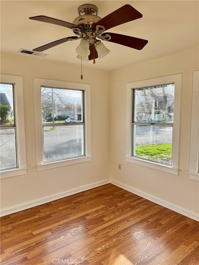 spare room with plenty of natural light, wood finished floors, visible vents, and baseboards