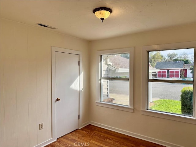 spare room with visible vents, plenty of natural light, baseboards, and wood finished floors