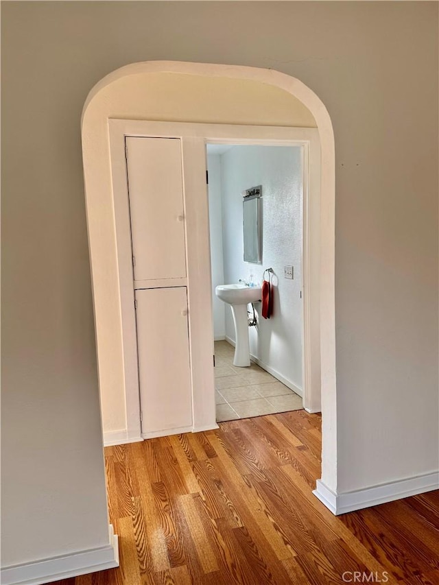 corridor with arched walkways, a sink, baseboards, and wood finished floors